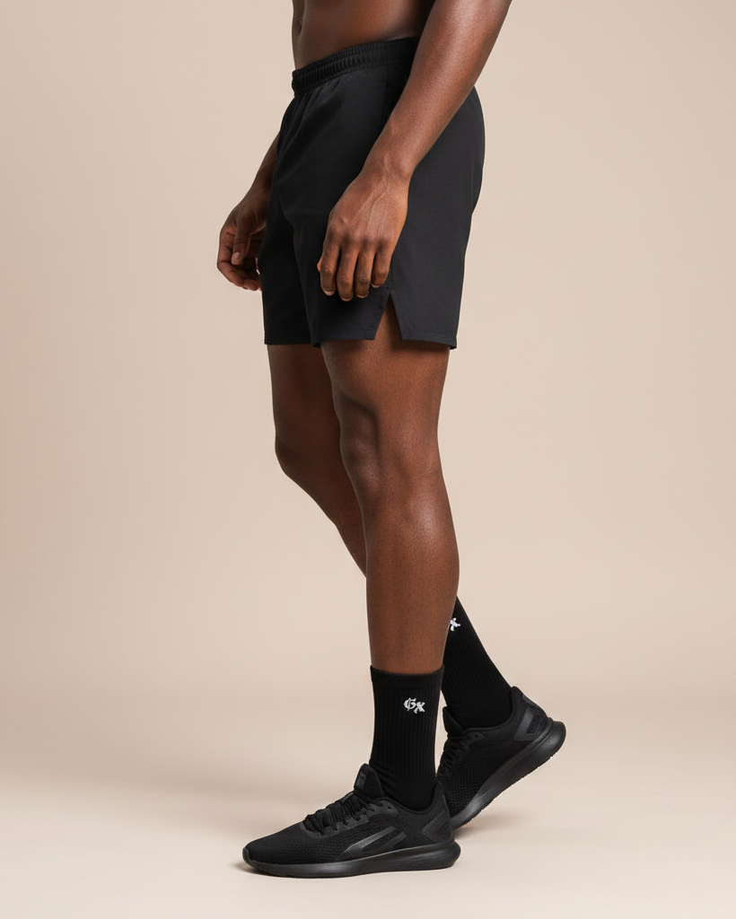 Person wearing black athletic shorts, socks, and shoes on a beige background