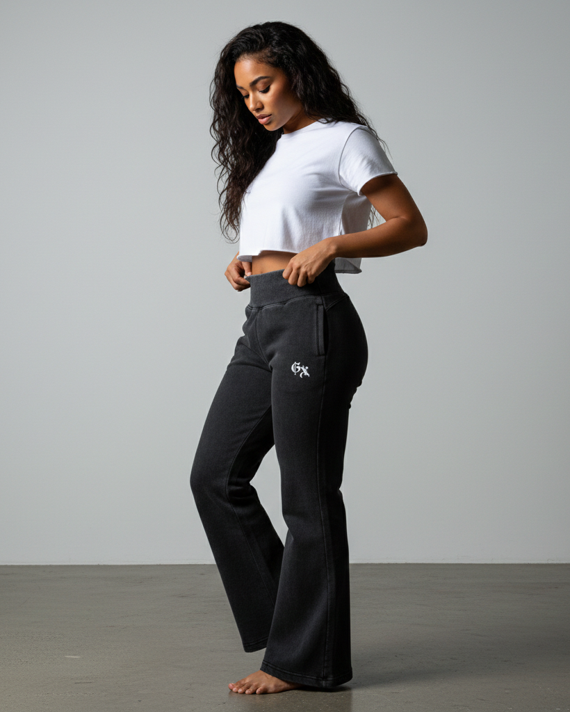 Woman wearing black pants with a logo and a white crop top on a gray background