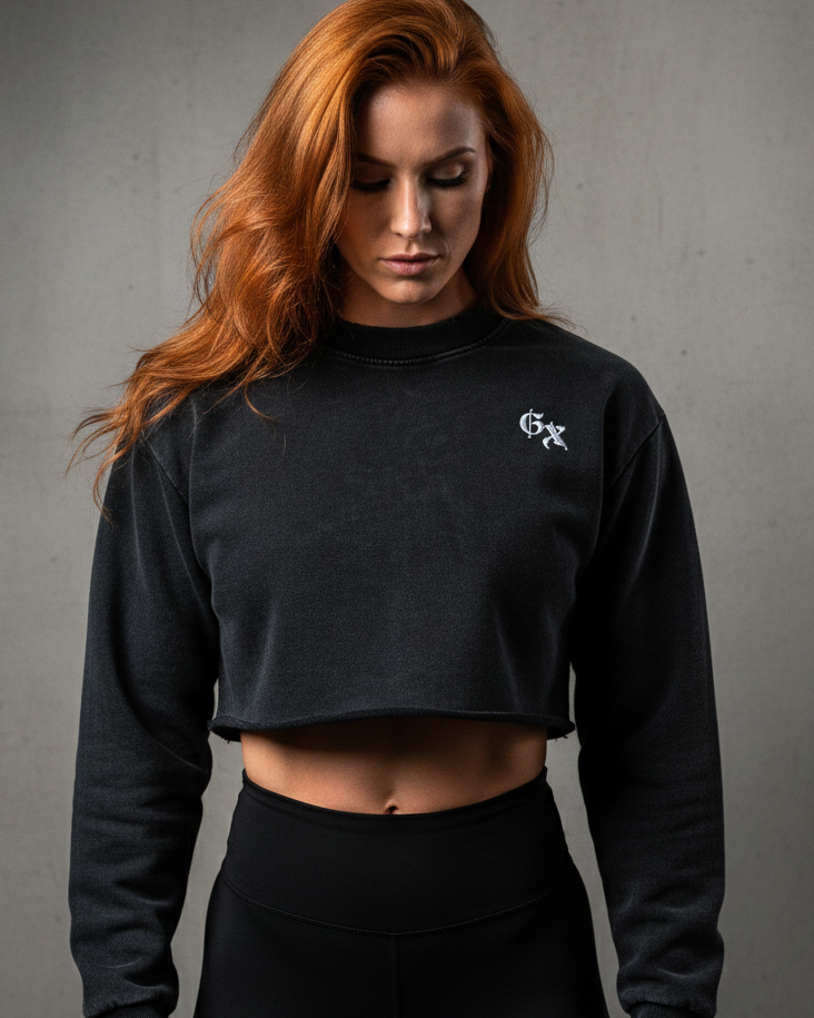 Woman wearing a black cropped sweatshirt with a logo on a gray background